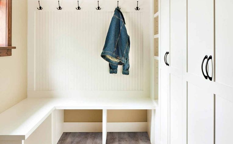 wood look flooring in mudroom with white storage bench and hangers.